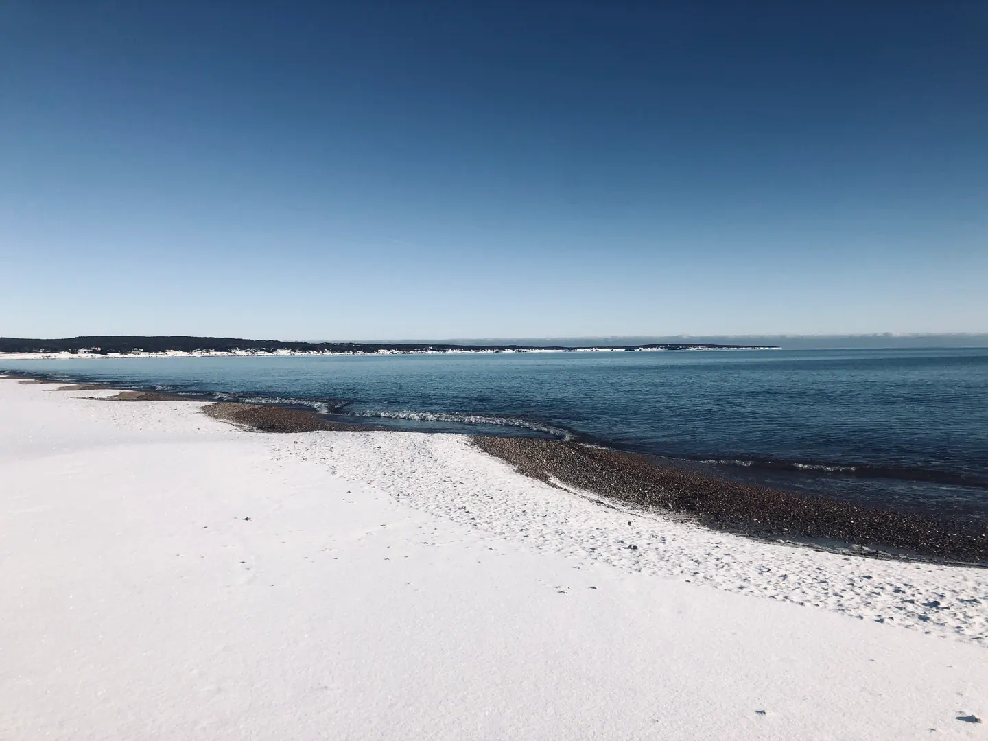 Plage enneigée bordant une mer turquoise, en Gaspésie